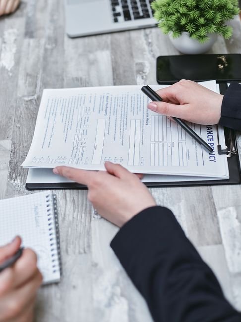 pexels photo 7731326 7731326 Close-up of hands analyzing insurance policy paperwork with pen on table.